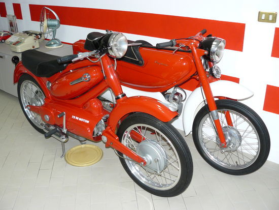 Nella seconda metà degli anni Cinquanta alcune case italiane hanno proposto interessanti moto con la meccanica completamente racchiusa dalla “carrozzeria”. Qui vediamo una Parilla Slughi (nella versione con motore a due tempi) a fianco di una Motom 98 TS, in primo piano